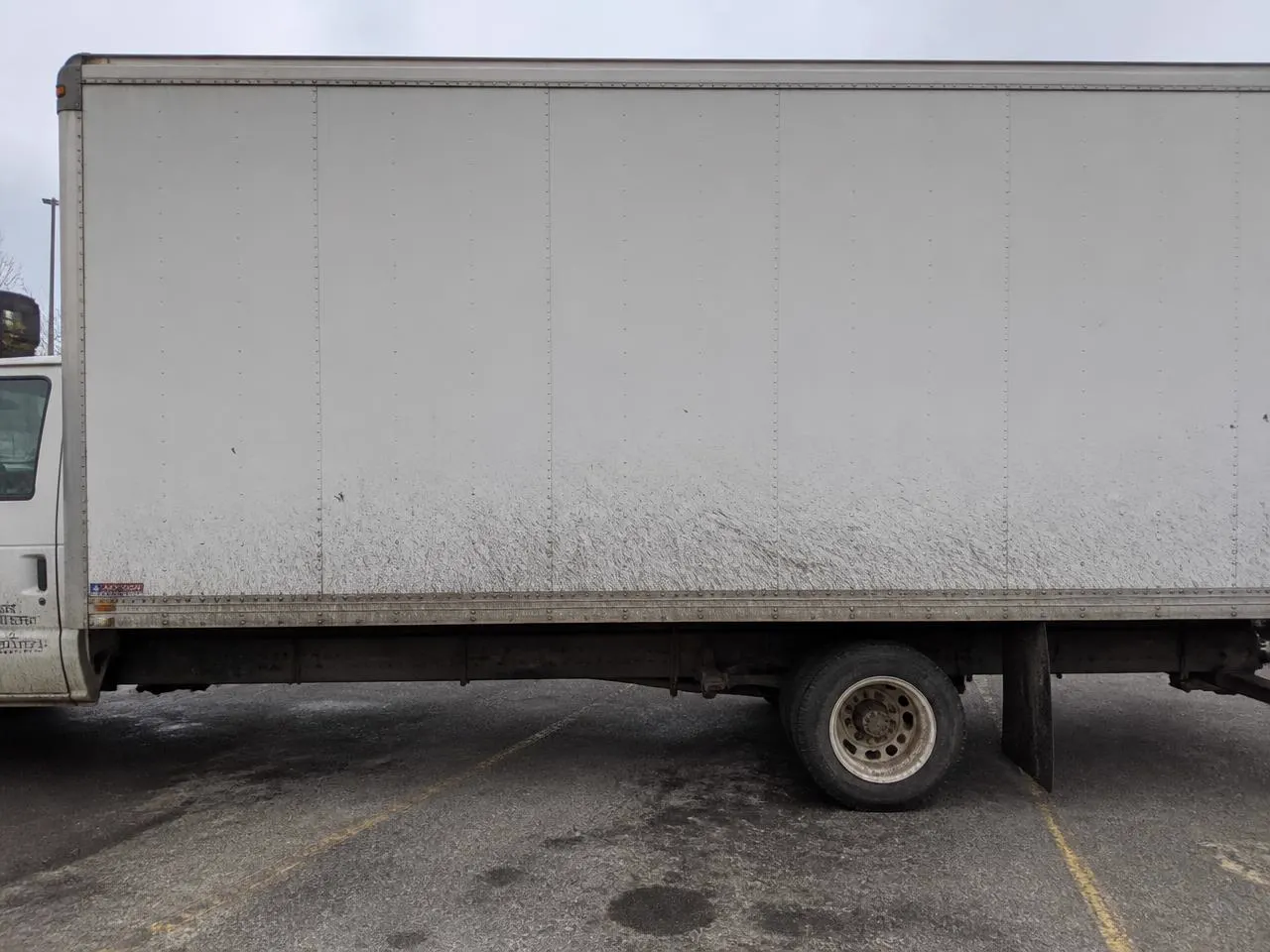 White box truck panel covered in road film, brake dust and dried mud